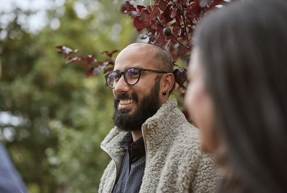 Man in glasses smiles while spending time outdoors with peers